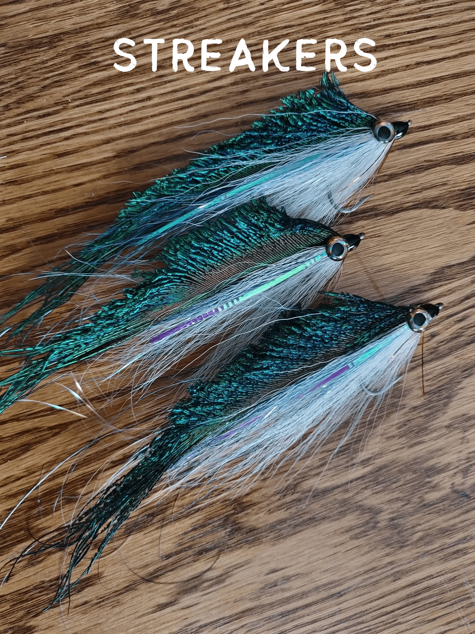 Three colorful fishing lures with feathered tails on a wooden surface.