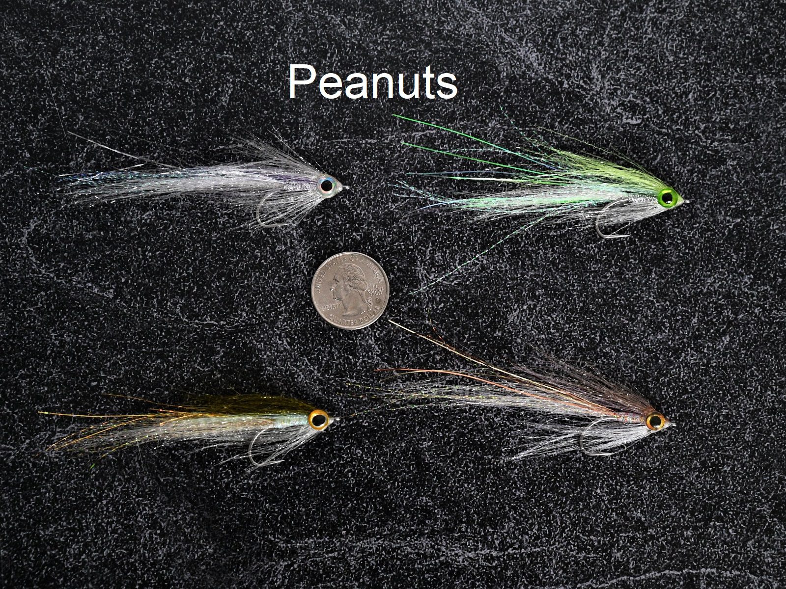 Four fishing flies arranged around a peanut on a dark surface.